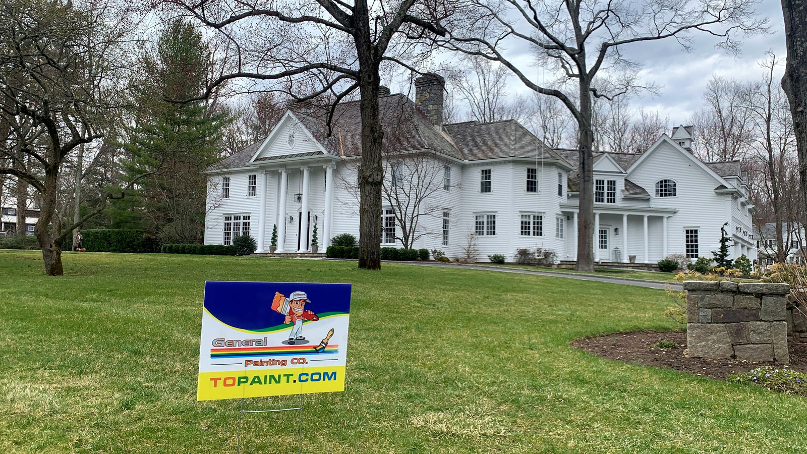 White colonial mansion with manicured lawn and General Painting Co. yard sign — finished exterior repaint