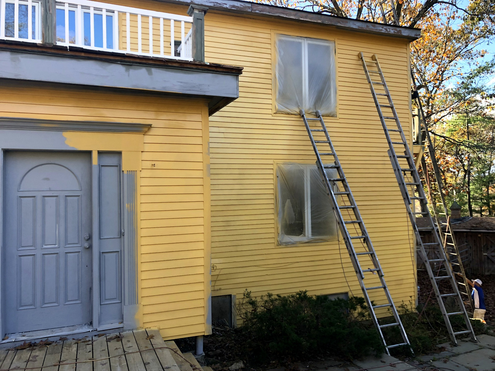 Yellow Connecticut home being repainted in summer with ladders staged