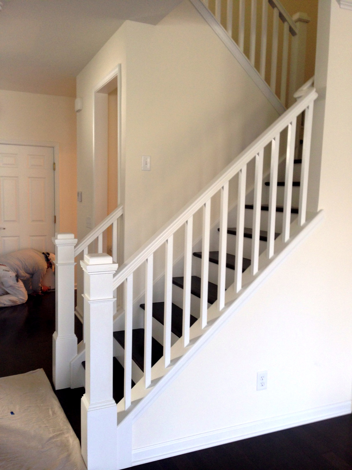 Crisp white painted staircase newel post and balusters with painter working in background, Connecticut interior project